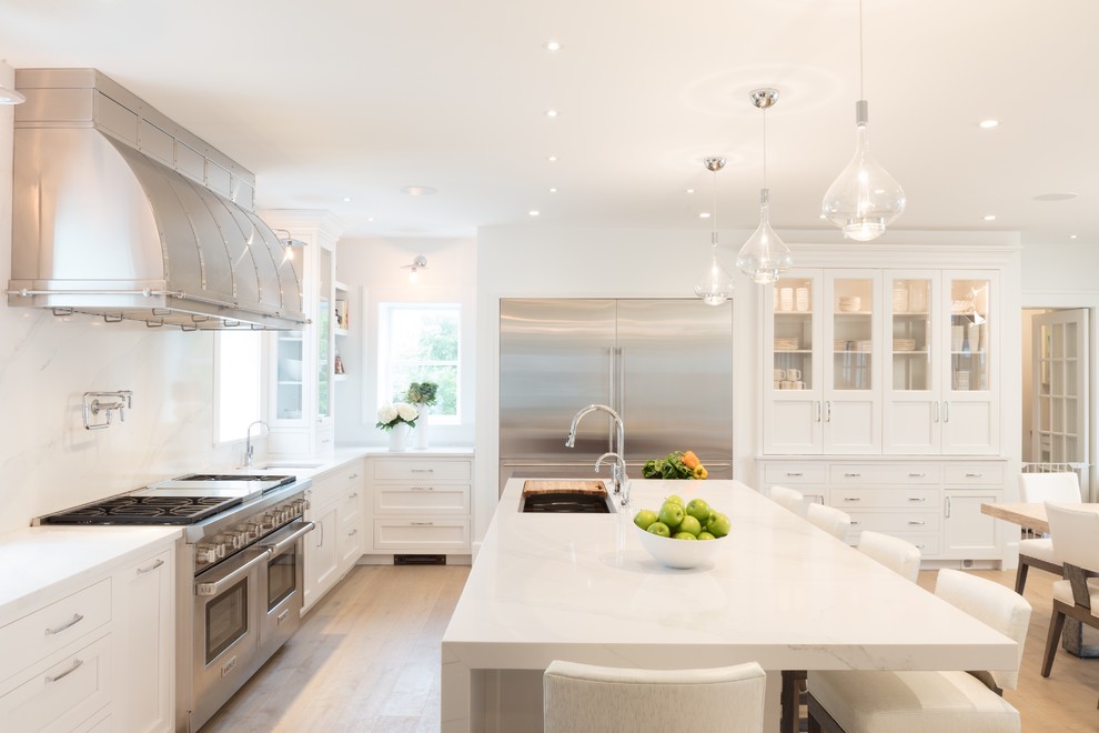 This is an example of a large beach style eat-in kitchen in Philadelphia with an undermount sink, white cabinets, white splashback, stainless steel appliances, light hardwood floors, with island, quartz benchtops, white benchtop and shaker cabinets.