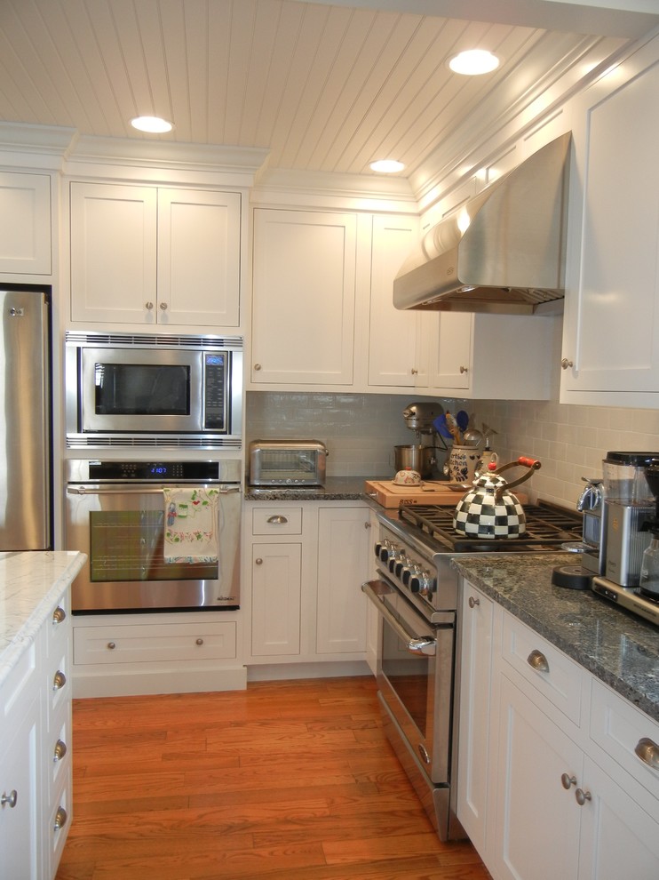 Example of a large transitional u-shaped medium tone wood floor open concept kitchen design with a farmhouse sink, shaker cabinets, white cabinets, granite countertops, subway tile backsplash, stainless steel appliances, an island and white backsplash