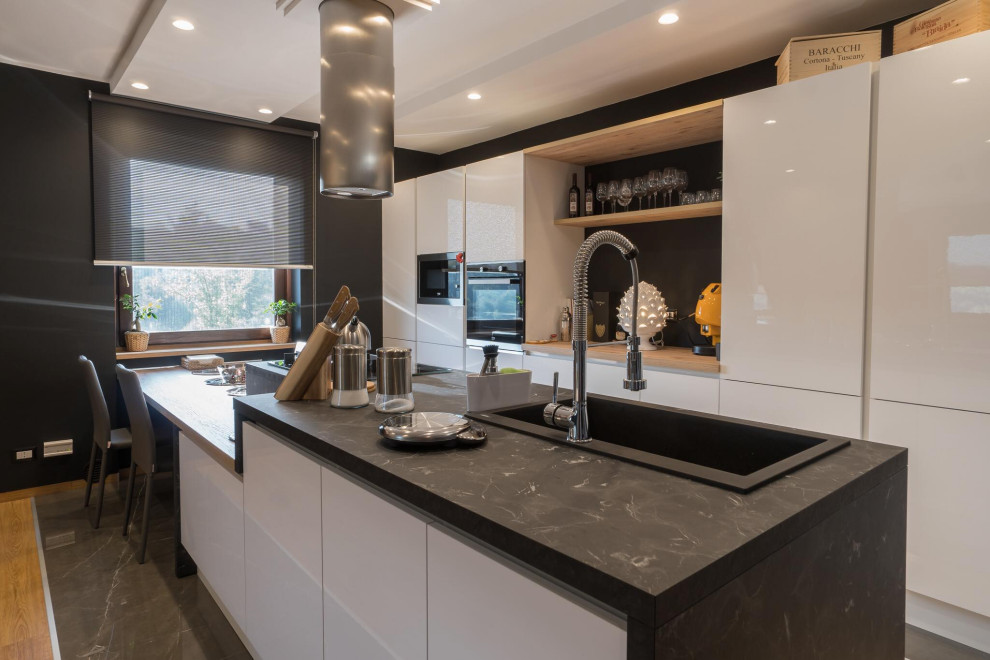 Inspiration for a mid-sized contemporary galley kitchen in Rome with a drop-in sink, flat-panel cabinets, white cabinets, black splashback, porcelain splashback, black appliances, a peninsula, grey floor and black benchtop.