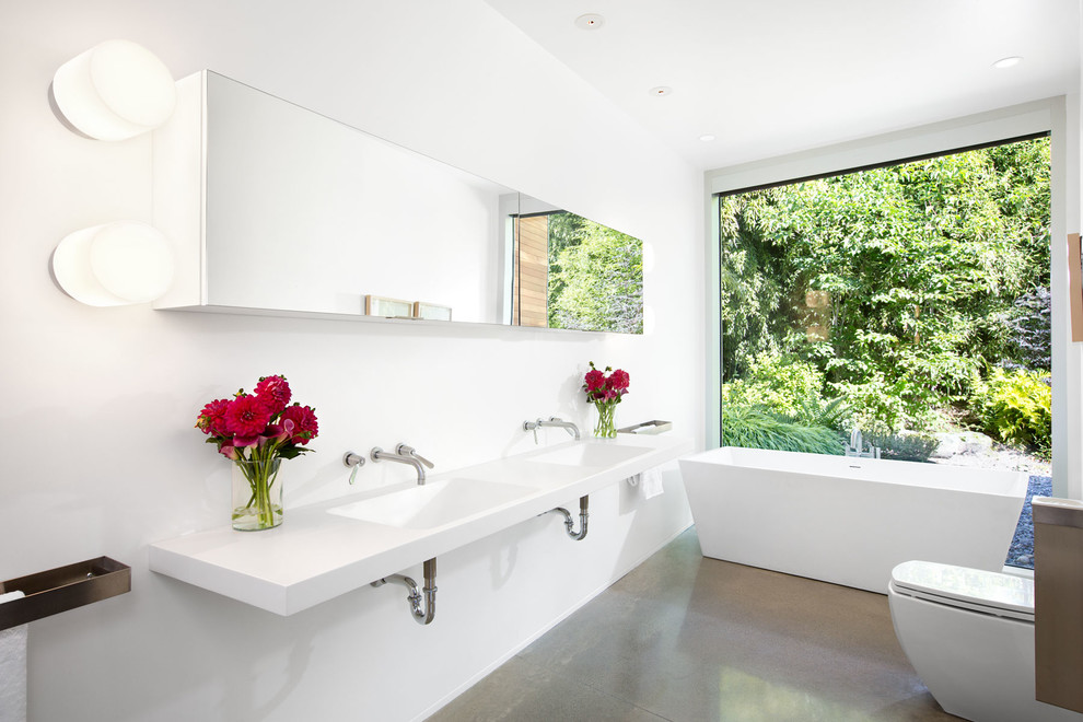 This is an example of a mid-sized contemporary master bathroom in Vancouver with a wall-mount sink, a freestanding tub, white walls and concrete floors.