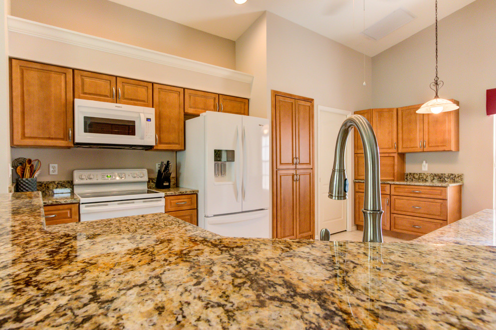 Example of a mid-sized kitchen design with an undermount sink, raised-panel cabinets, medium tone wood cabinets, granite countertops, white appliances and brown countertops