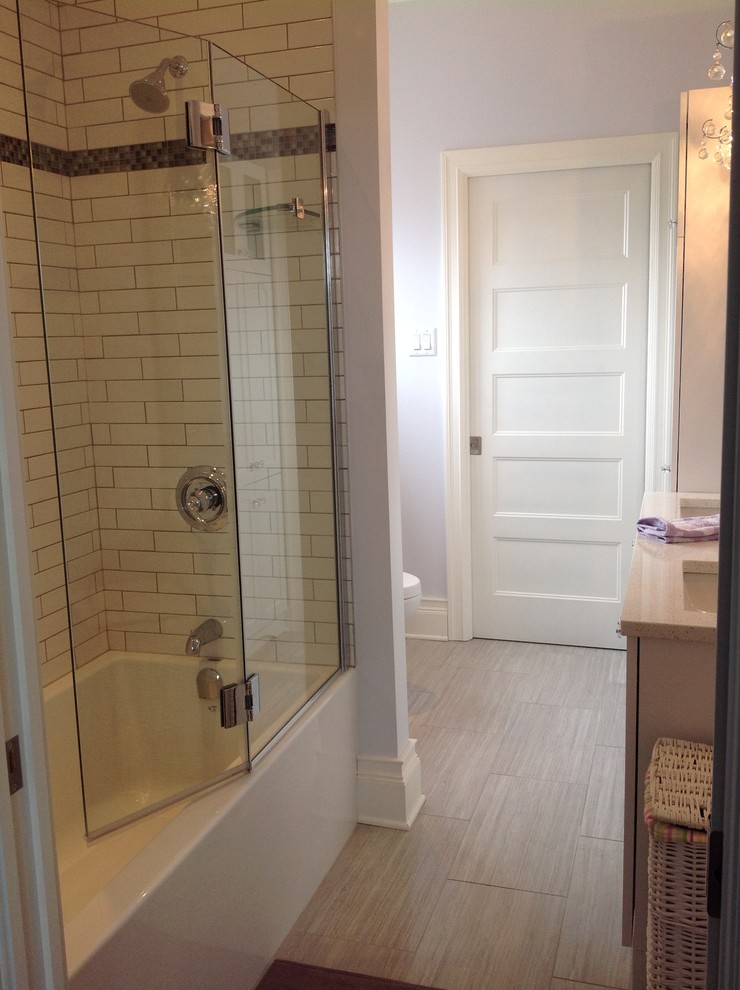 This is an example of a mid-sized traditional bathroom in Montreal with an undermount sink, shaker cabinets, white cabinets, engineered quartz benchtops, an alcove tub, a shower/bathtub combo, a one-piece toilet, gray tile, porcelain tile, grey walls and porcelain floors.
