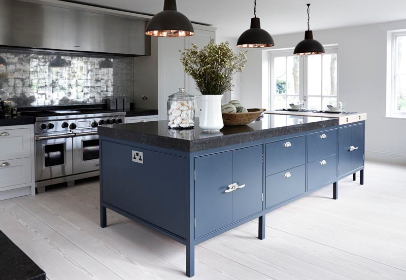 This is an example of a large contemporary galley eat-in kitchen in London with a drop-in sink, shaker cabinets, blue cabinets, solid surface benchtops, metallic splashback, metal splashback, stainless steel appliances, medium hardwood floors, with island and black benchtop.
