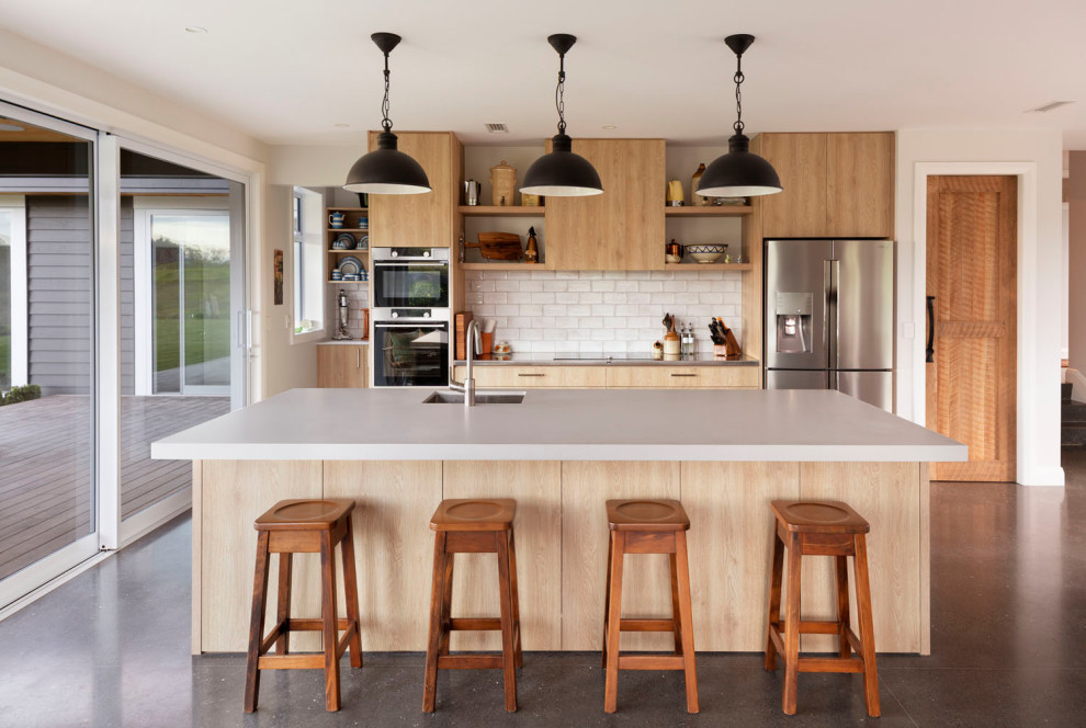 This is an example of a large contemporary single-wall kitchen/diner in Auckland with a built-in sink, flat-panel cabinets, medium wood cabinets, engineered stone countertops, grey splashback, ceramic splashback, stainless steel appliances, concrete flooring, an island, grey floors and white worktops.