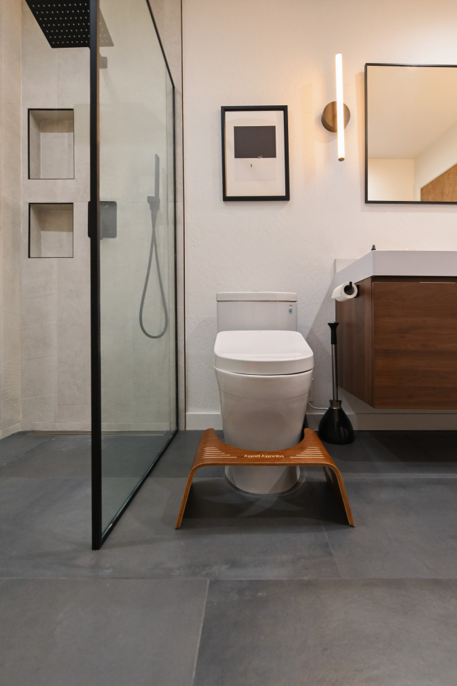 This is an example of a small contemporary 3/4 bathroom in Austin with flat-panel cabinets, medium wood cabinets, an alcove shower, a one-piece toilet, gray tile, ceramic tile, ceramic floors, marble benchtops, grey floor, a hinged shower door, white benchtops, a niche, a single vanity, a floating vanity, panelled walls and beige walls.