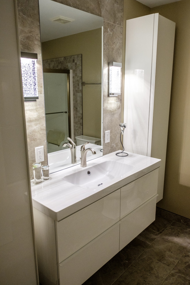 Photo of a mid-sized contemporary master bathroom in Edmonton with white cabinets, a two-piece toilet, ceramic tile, beige walls, multi-coloured floor, a single vanity, flat-panel cabinets, an alcove tub, a shower/bathtub combo, multi-coloured tile, ceramic floors, an integrated sink, solid surface benchtops, a sliding shower screen, white benchtops and a floating vanity.