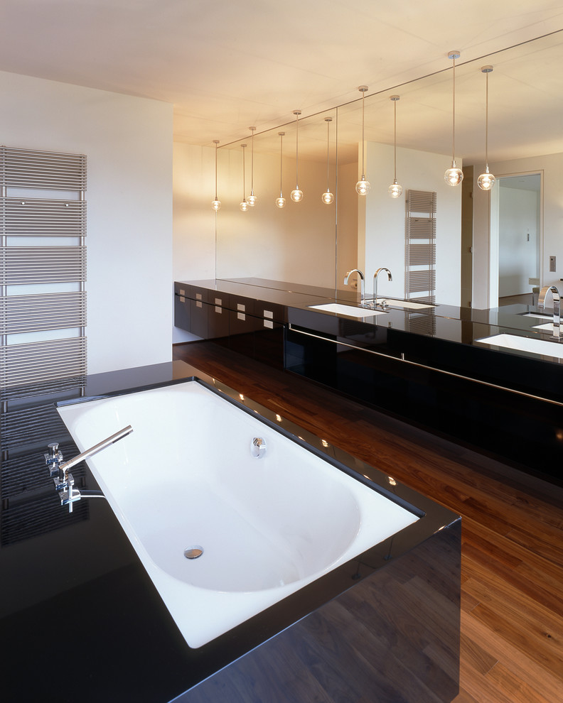 Photo of a large contemporary bathroom in Bremen with flat-panel cabinets, black cabinets, a drop-in tub, white walls, dark hardwood floors and an integrated sink.
