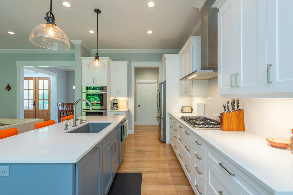 Kitchen - mid-sized transitional l-shaped light wood floor and brown floor kitchen idea with an undermount sink, shaker cabinets, white cabinets, quartzite countertops, white backsplash, ceramic backsplash, stainless steel appliances, an island and white countertops