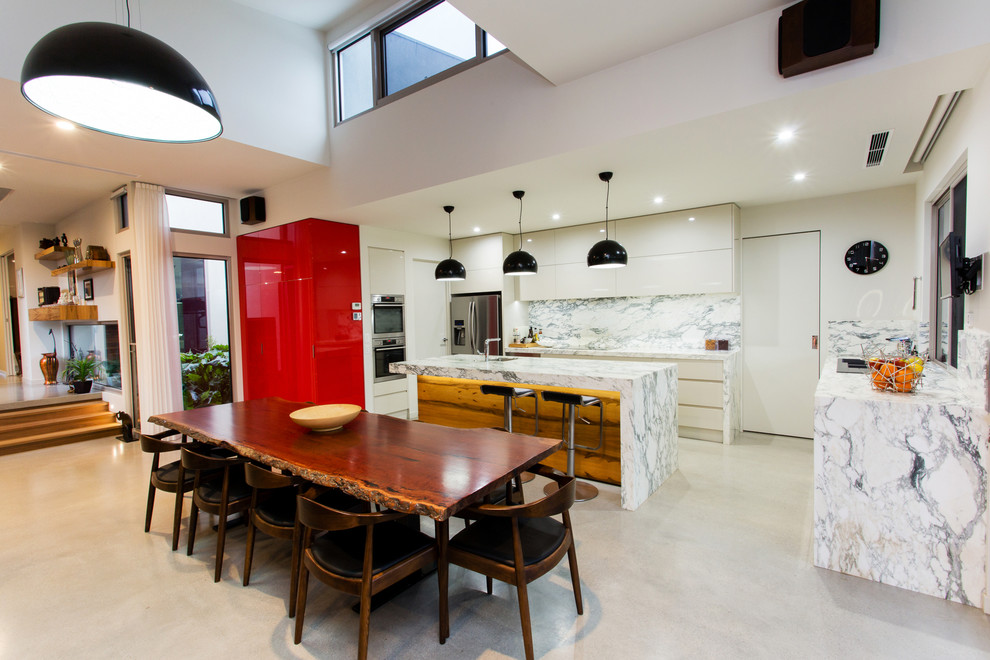Design ideas for a contemporary l-shaped eat-in kitchen in Geelong with flat-panel cabinets, white cabinets, marble benchtops, white splashback, stone slab splashback, stainless steel appliances, concrete floors, with island and a drop-in sink.