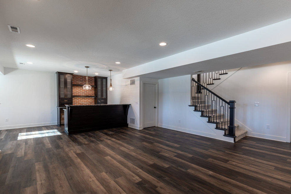 This is an example of a large modern look-out basement in Kansas City with a home bar, white walls, dark hardwood floors, no fireplace, brown floor and vaulted.