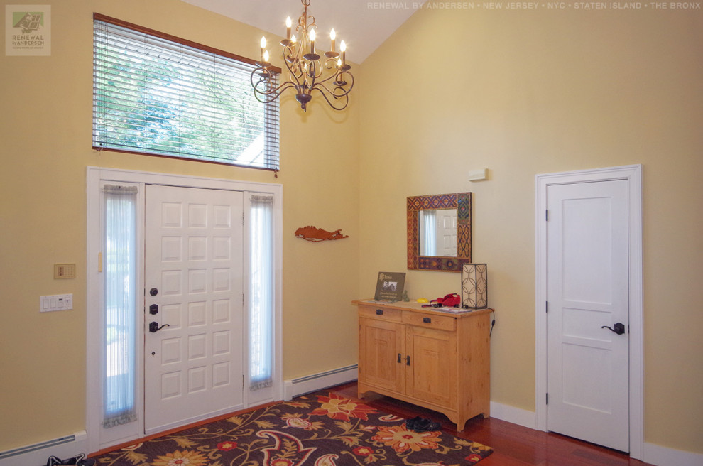 Ejemplo de distribuidor abovedado de tamaño medio con paredes amarillas, suelo de madera en tonos medios, puerta simple, puerta blanca y suelo multicolor