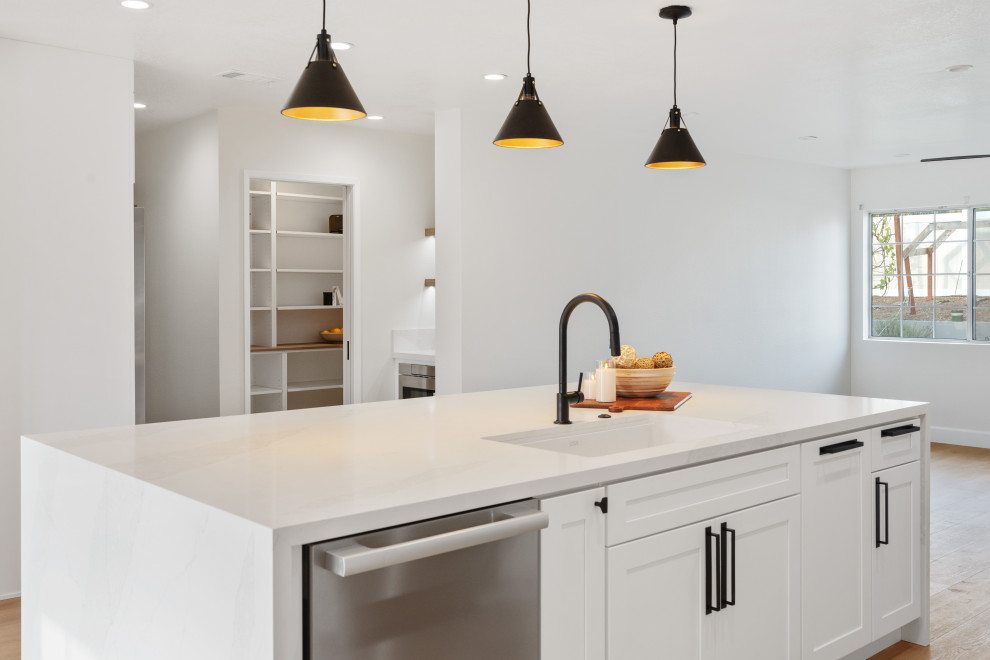 Example of a mid-sized transitional vinyl floor and brown floor open concept kitchen design in Orange County with an undermount sink, shaker cabinets, white cabinets, quartz countertops, white backsplash, quartz backsplash, stainless steel appliances, an island and white countertops