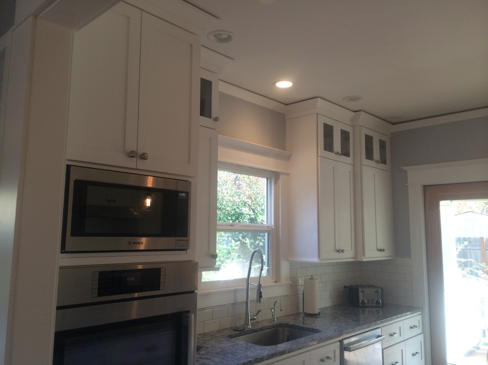 Large transitional u-shaped eat-in kitchen in Portland with an undermount sink, recessed-panel cabinets, white cabinets, granite benchtops, white splashback, subway tile splashback, stainless steel appliances, medium hardwood floors and with island.