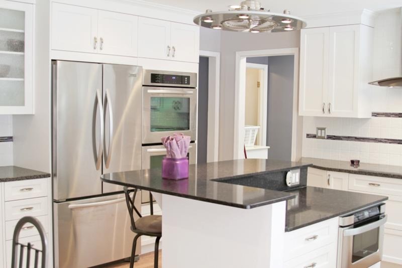 This is an example of a mid-sized eclectic u-shaped eat-in kitchen in St Louis with shaker cabinets, white cabinets, quartz benchtops, white splashback, matchstick tile splashback, stainless steel appliances, medium hardwood floors and with island.