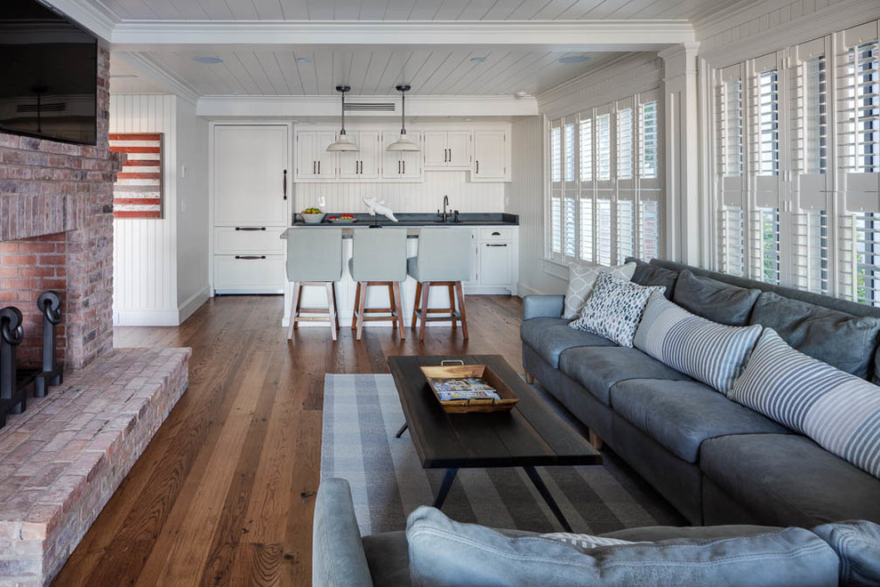 This is an example of a mid-sized beach style open concept family room in Boston with white walls, medium hardwood floors, a brick fireplace surround, a wall-mounted tv, a home bar and a standard fireplace.