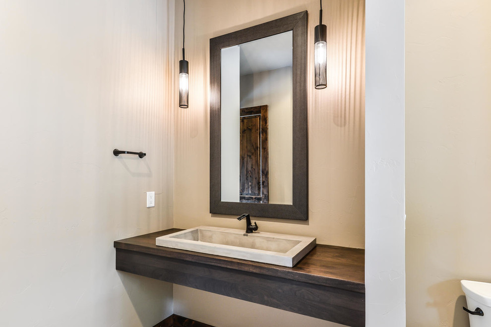 This is an example of a mid-sized contemporary powder room in Denver with a two-piece toilet, beige walls, a drop-in sink, wood benchtops, beige floor and brown benchtops.