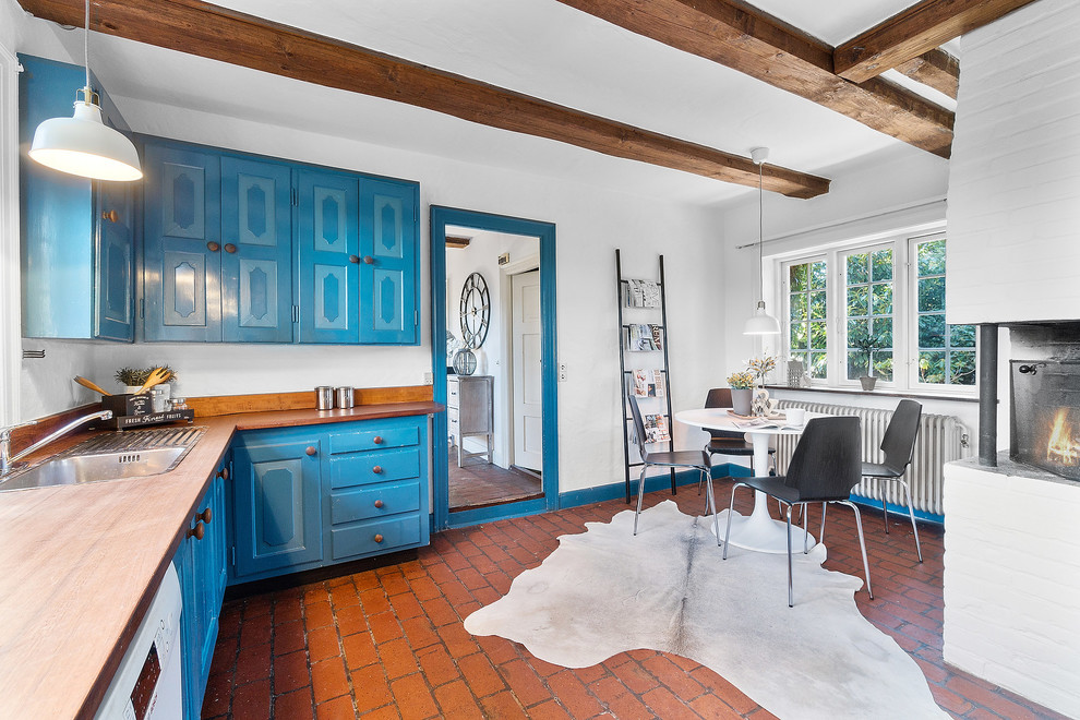 Inspiration for a mid-sized country l-shaped eat-in kitchen in Copenhagen with beaded inset cabinets, blue cabinets, wood benchtops, brick floors, no island, brown benchtop, a drop-in sink, white appliances and red floor.