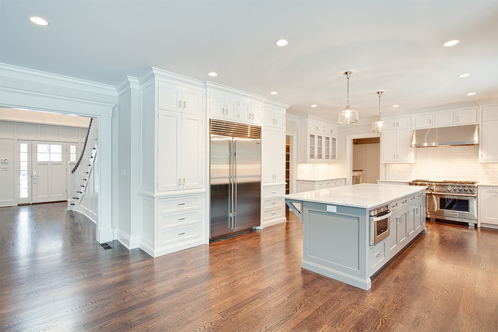 Large transitional u-shaped dark wood floor and brown floor eat-in kitchen photo with an undermount sink, shaker cabinets, white cabinets, white backsplash, stainless steel appliances and an island