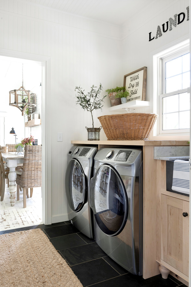Inspiration for a country laundry room in Minneapolis with shaker cabinets, light wood cabinets, wood benchtops, white walls, a side-by-side washer and dryer, black floor and beige benchtop.