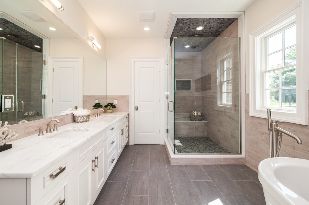 Transitional master bathroom in New York with white cabinets, porcelain floors, engineered quartz benchtops, recessed-panel cabinets, a freestanding tub, a corner shower, beige tile, black tile, gray tile, pebble tile, beige walls, an undermount sink and a hinged shower door.