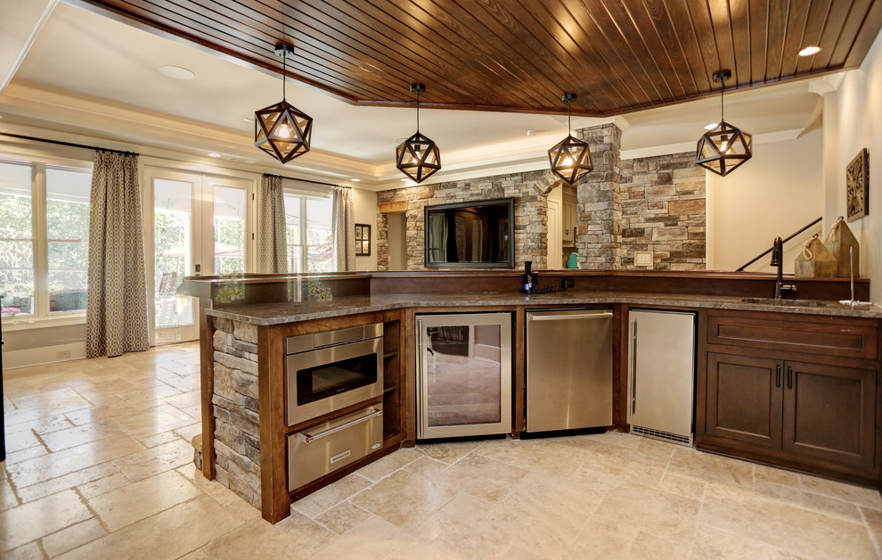 This is an example of a large traditional u-shaped home bar in Atlanta with an undermount sink, raised-panel cabinets, brown cabinets, granite benchtops, grey splashback, travertine floors and brown floor.
