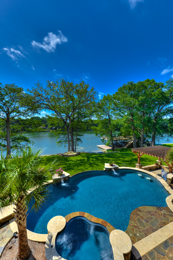Large mediterranean backyard custom-shaped infinity pool in Austin with a hot tub and natural stone pavers.