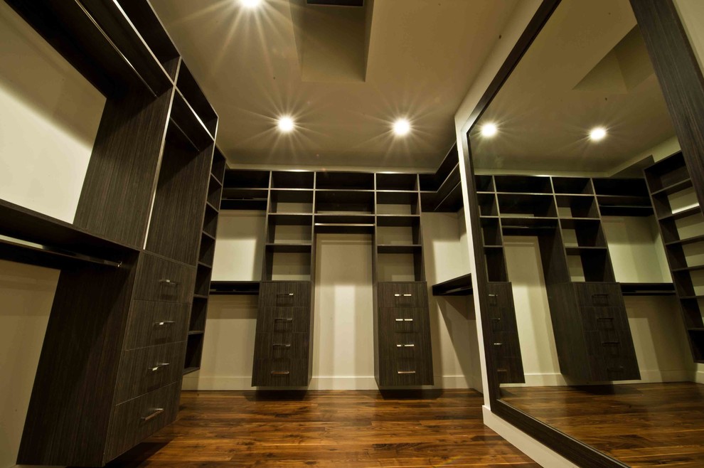 This is an example of a large modern gender-neutral walk-in wardrobe in Calgary with flat-panel cabinets, dark wood cabinets and medium hardwood floors.