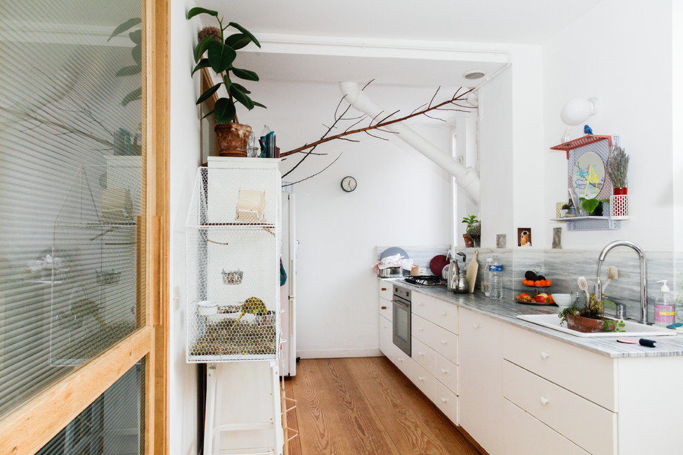 Exemple d'une cuisine parallèle tendance fermée et de taille moyenne avec une crédence grise et un sol en bois brun.