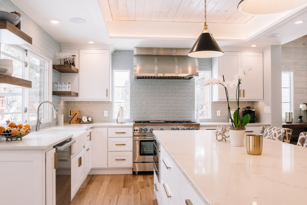 Mid-sized transitional l-shaped eat-in kitchen in Denver with a farmhouse sink, shaker cabinets, white cabinets, grey splashback, stainless steel appliances, medium hardwood floors, with island, brown floor, white benchtop, recessed, quartz benchtops and glass tile splashback.