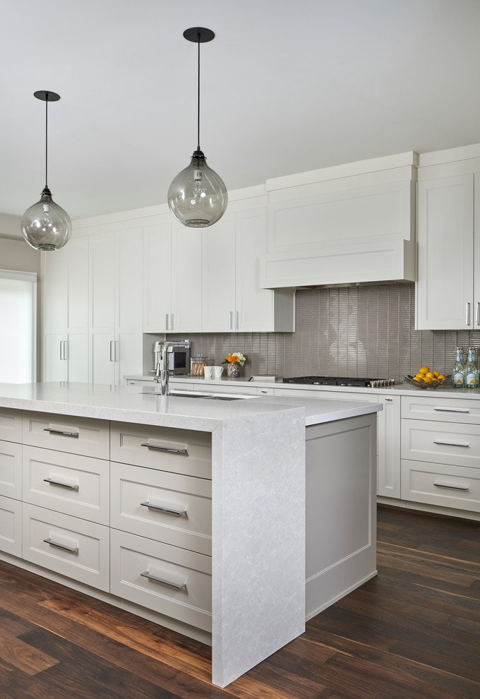 Mid-sized transitional l-shaped medium tone wood floor and brown floor eat-in kitchen photo in Toronto with a double-bowl sink, shaker cabinets, white cabinets, quartz countertops, brown backsplash, glass tile backsplash, stainless steel appliances, an island and white countertops