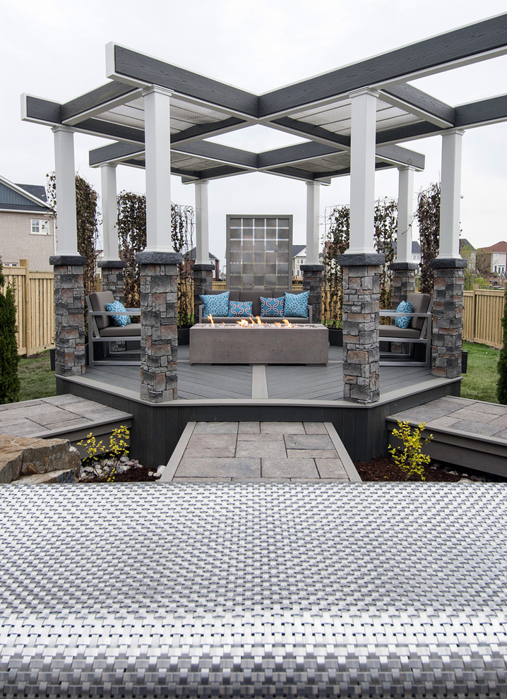 Design ideas for a mid-sized industrial backyard deck in Toronto with a fire feature and a pergola.