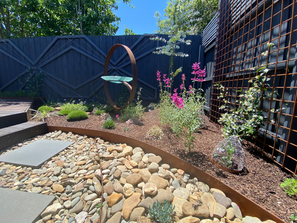 Kleiner, Halbschattiger Moderner Garten im Frühling, hinter dem Haus mit Wasserspiel, Flusssteinen und Holzzaun in Melbourne