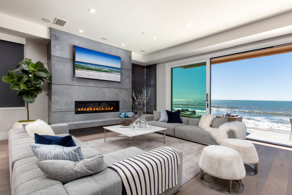 Photo of a mid-sized beach style open concept family room in Orange County with grey walls, light hardwood floors, a ribbon fireplace, a wall-mounted tv, a concrete fireplace surround and brown floor.