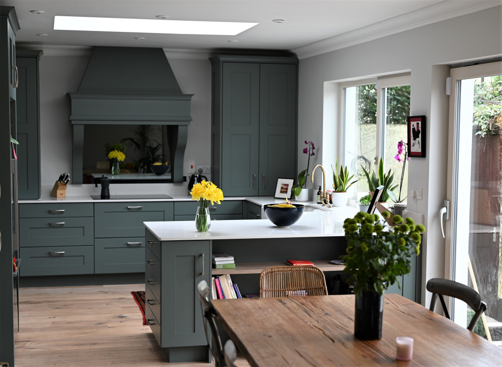 Design ideas for a mid-sized contemporary u-shaped eat-in kitchen in Dublin with a farmhouse sink, recessed-panel cabinets, green cabinets, marble benchtops, white splashback, marble splashback, stainless steel appliances, light hardwood floors, a peninsula, brown floor and white benchtop.
