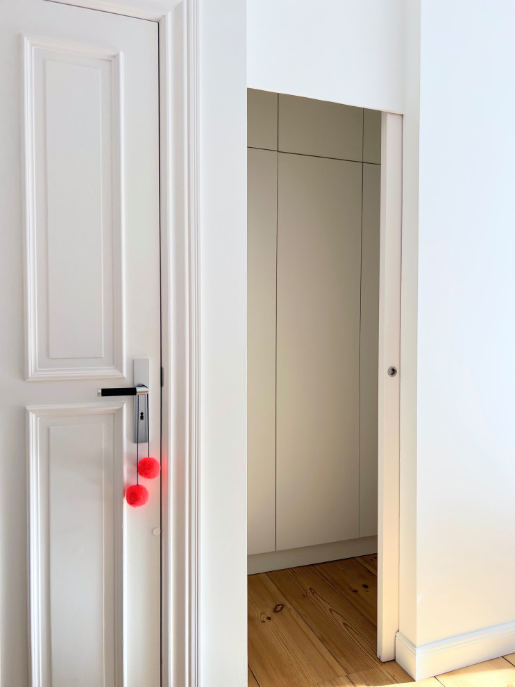 Exemple d'une petite buanderie tendance en L avec un placard, un placard à porte plane, des portes de placard blanches, un mur blanc, parquet clair et un sol marron.