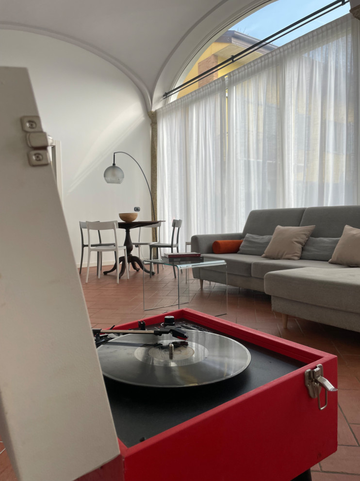 На фото: большая изолированная гостиная комната в современном стиле с белыми стенами, полом из терракотовой плитки, мультимедийным центром, красным полом и сводчатым потолком