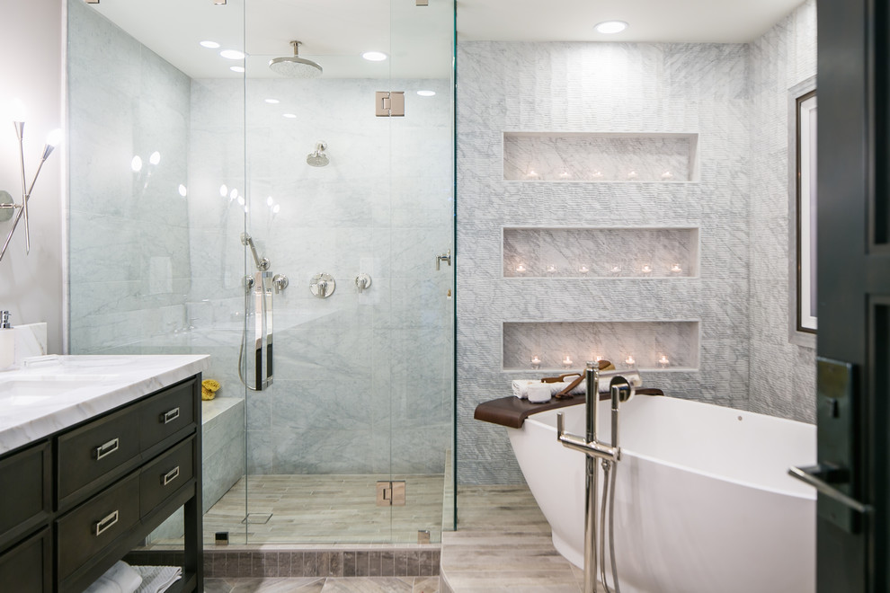 This is an example of a mid-sized transitional master bathroom in Denver with a two-piece toilet, gray tile, marble, grey walls, porcelain floors, an undermount sink, quartzite benchtops, grey floor, a hinged shower door, black cabinets, a freestanding tub, a curbless shower and recessed-panel cabinets.