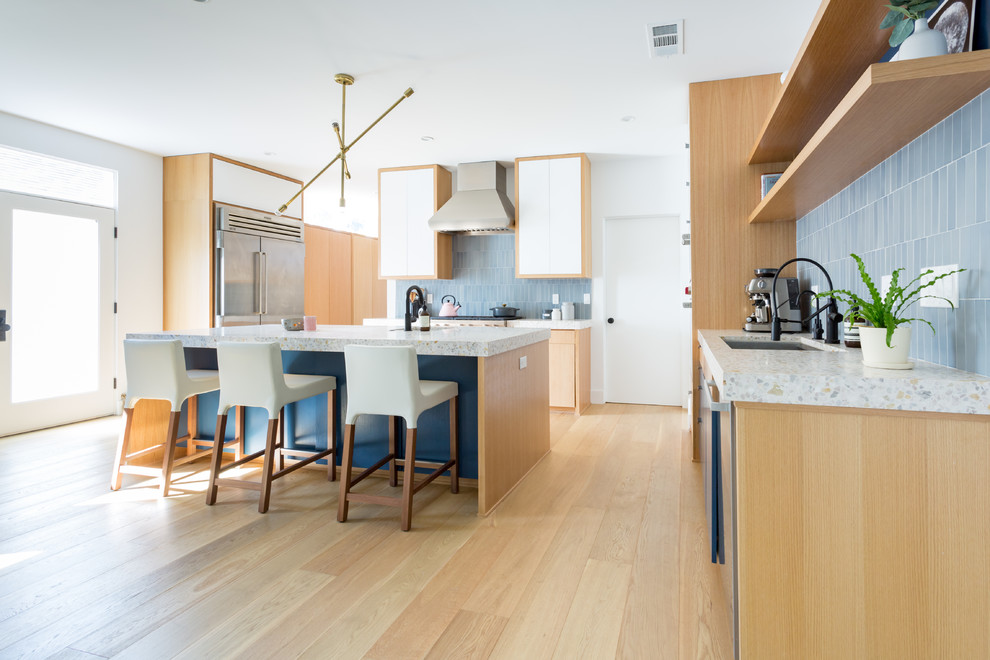 Photo of a large midcentury galley open plan kitchen in Los Angeles with an undermount sink, flat-panel cabinets, blue cabinets, concrete benchtops, blue splashback, ceramic splashback, stainless steel appliances, light hardwood floors and with island.