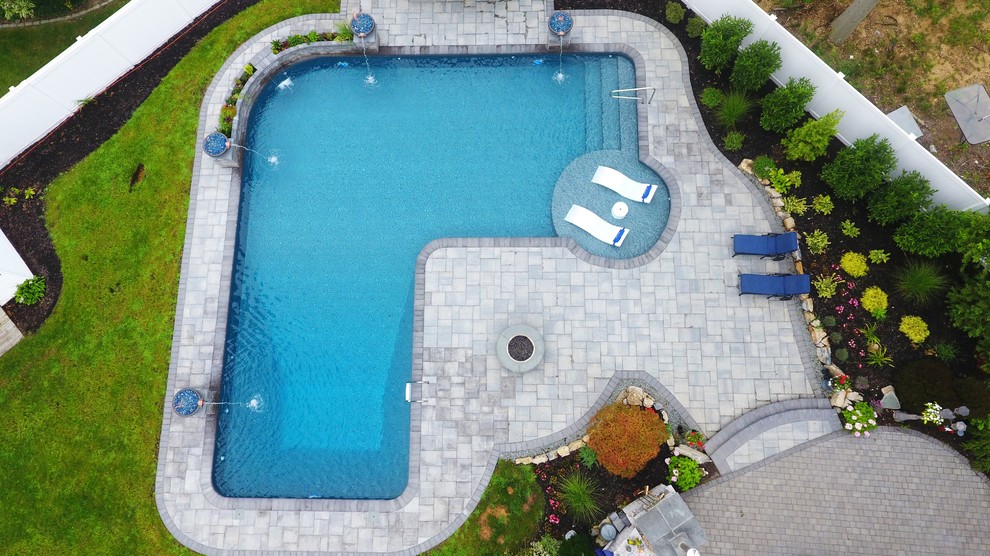 Photo of a large backyard l-shaped pool in New York with a water feature and concrete pavers.