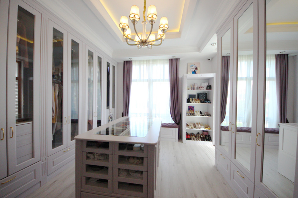 This is an example of a large eclectic women's walk-in wardrobe in Moscow with recessed-panel cabinets, light wood cabinets, medium hardwood floors, beige floor and recessed.