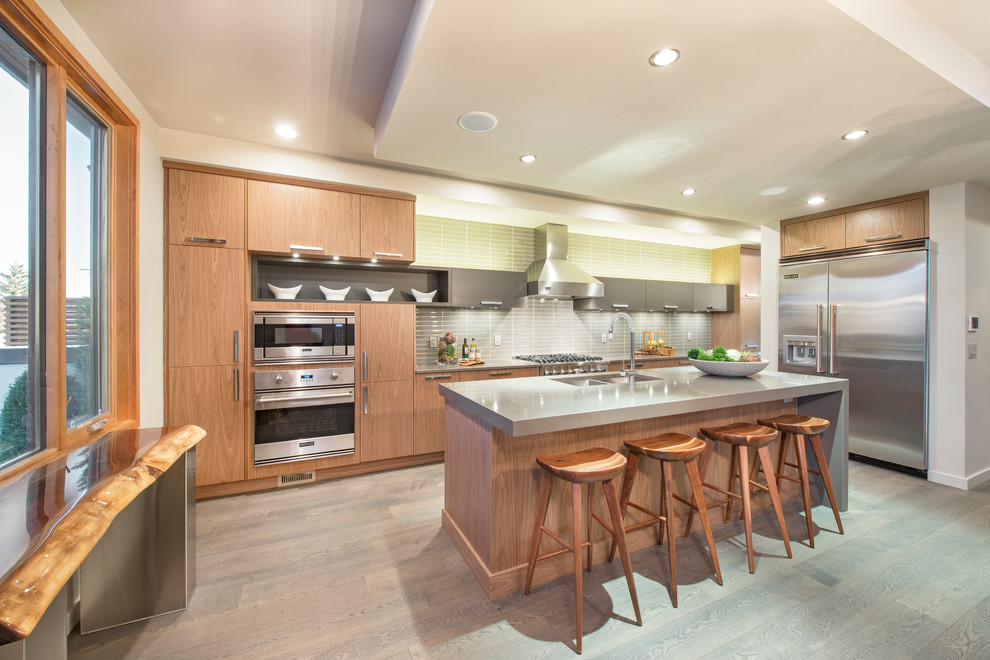 Kitchen - transitional light wood floor kitchen idea in Calgary with an undermount sink, flat-panel cabinets, light wood cabinets, quartzite countertops, green backsplash, glass tile backsplash, stainless steel appliances and an island