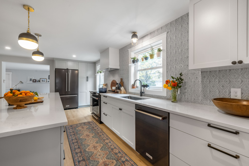 This is an example of a mid-sized transitional galley eat-in kitchen in Portland Maine with an undermount sink, shaker cabinets, white cabinets, quartz benchtops, blue splashback, porcelain splashback, stainless steel appliances, porcelain floors, with island, brown floor and white benchtop.