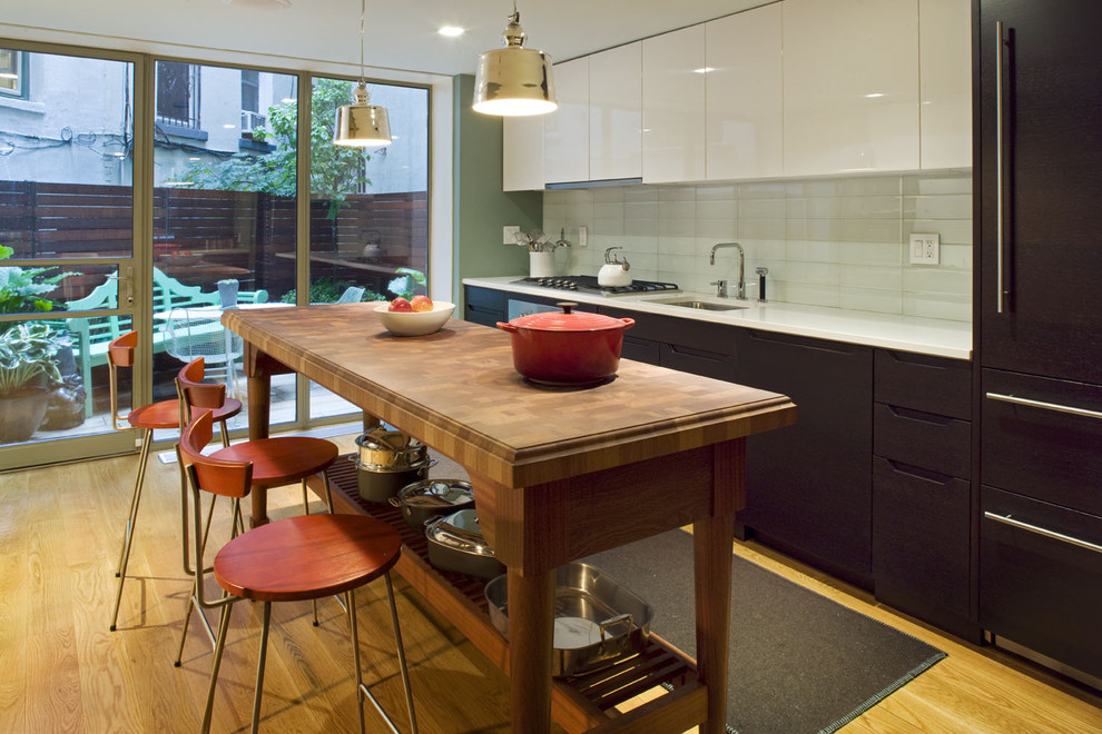 This is an example of a contemporary single-wall kitchen in New York with an undermount sink, flat-panel cabinets, dark wood cabinets, white splashback and subway tile splashback.