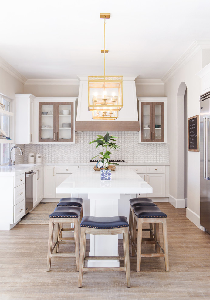 Inspiration for a beach style l-shaped kitchen in San Diego with shaker cabinets, white cabinets, stainless steel appliances, light hardwood floors, with island, beige floor and white benchtop.