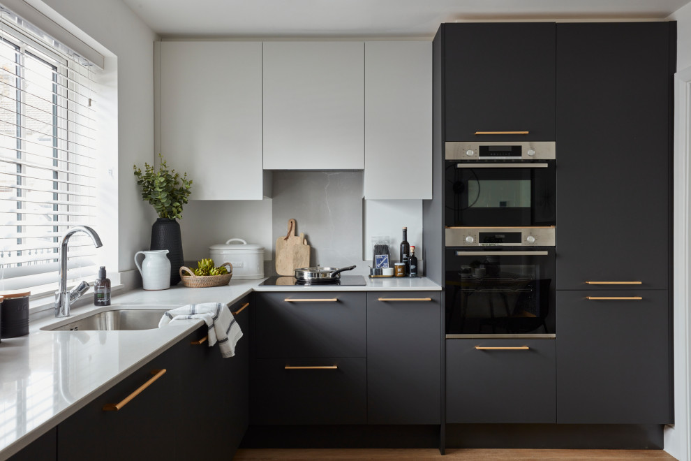 Design ideas for a mid-sized contemporary l-shaped separate kitchen in London with an undermount sink, flat-panel cabinets, black cabinets, grey splashback, panelled appliances, no island, brown floor and grey benchtop.