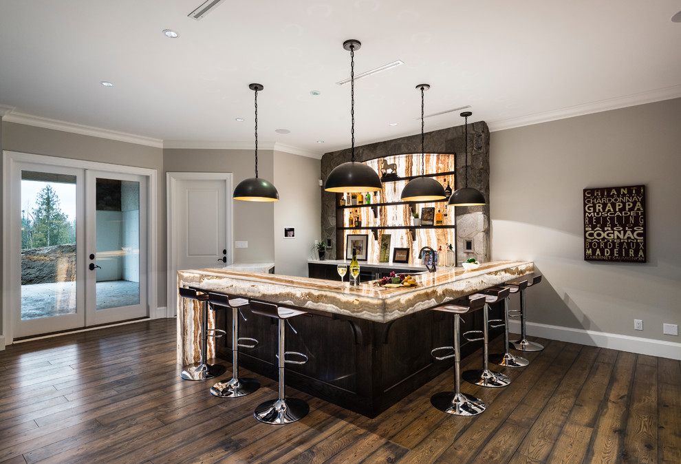 This is an example of an expansive country u-shaped wet bar in Vancouver with a drop-in sink, shaker cabinets, dark wood cabinets, onyx benchtops, beige splashback, stone slab splashback, medium hardwood floors, brown floor and beige benchtop.