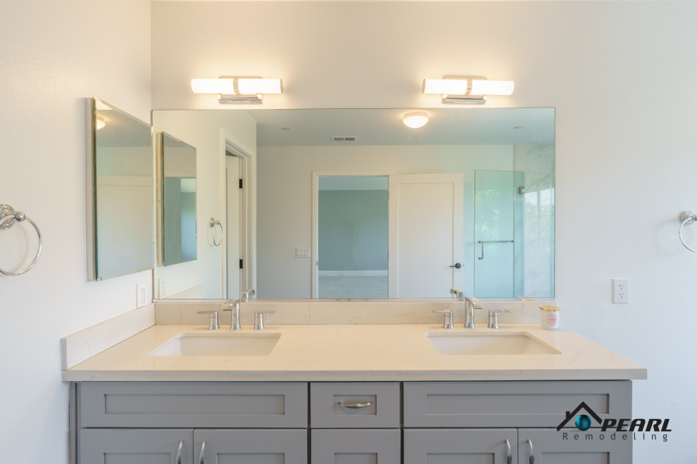 На фото: огромная главная ванная комната в стиле модернизм с фасадами в стиле шейкер, серыми фасадами, отдельно стоящей ванной, угловым душем, раздельным унитазом, белой плиткой, мраморной плиткой, бежевыми стенами, полом из керамической плитки, накладной раковиной, столешницей из искусственного камня, серым полом, душем с распашными дверями, бежевой столешницей, тумбой под две раковины и встроенной тумбой с