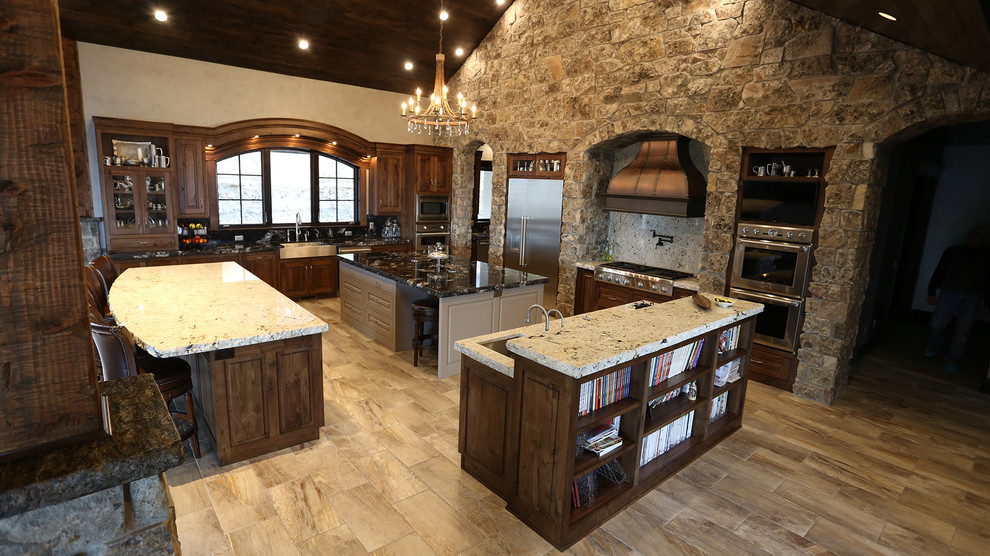 Expansive country u-shaped open plan kitchen in Salt Lake City with a farmhouse sink, recessed-panel cabinets, dark wood cabinets, granite benchtops, black splashback, stainless steel appliances and multiple islands.