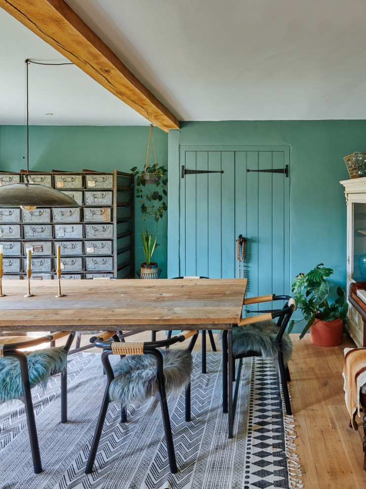 Modelo de comedor campestre de tamaño medio cerrado sin chimenea con paredes azules, suelo de madera en tonos medios, suelo marrón, vigas vistas y ladrillo