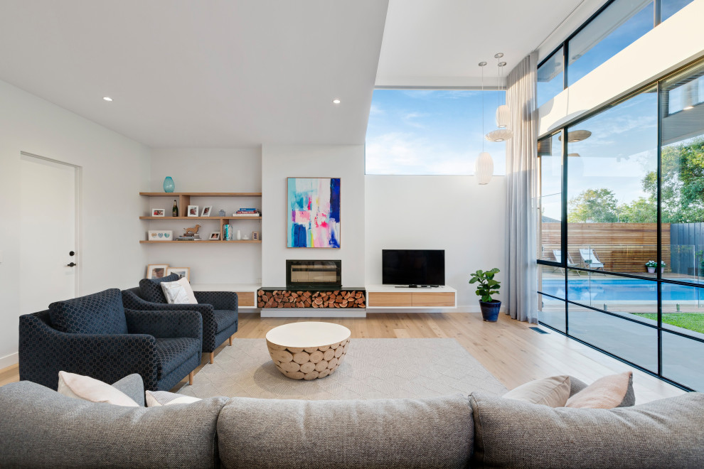 This is an example of a contemporary living room in Melbourne with white walls, light hardwood floors, a freestanding tv and beige floor.
